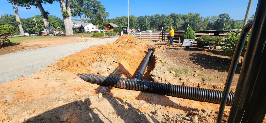 Construction site with workers installing drainage pipe in a trench under clear blue sky.