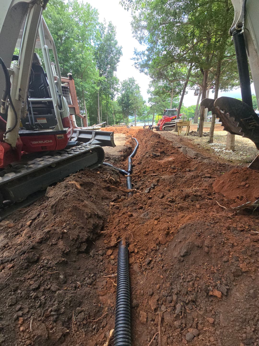 Excavation site with heavy machinery and trench for drainage installation in wooded area.