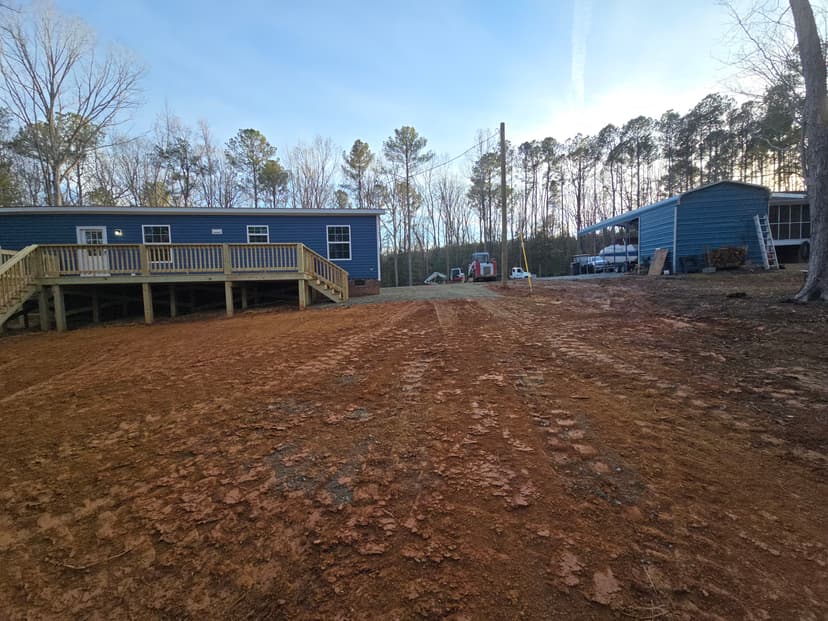 Newly built blue homes on a dirt lot surrounded by trees, showcasing outdoor space and construction.