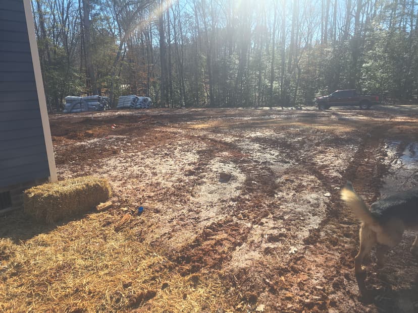 cleared land with straw bales, muddy ground, trees in background, and a parked truck