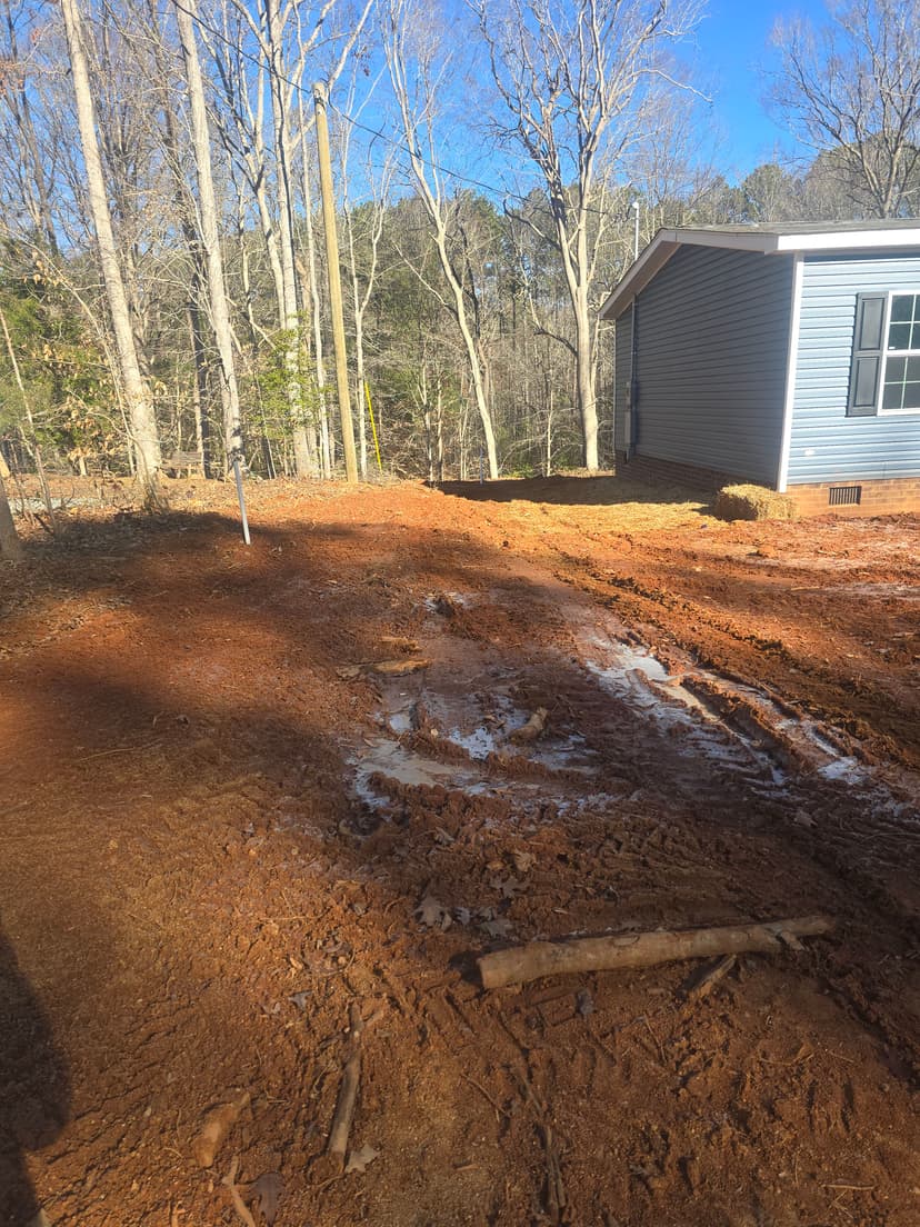 cleared dirt lot with muddy patches, trees in background, and house side visible