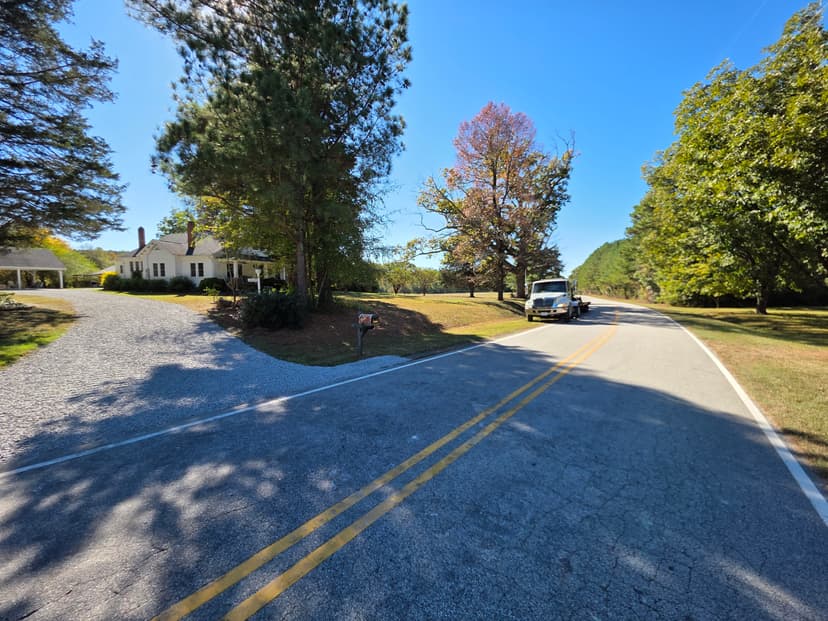 Gravel driveway and asphalt road with a truck near a house and colorful trees.