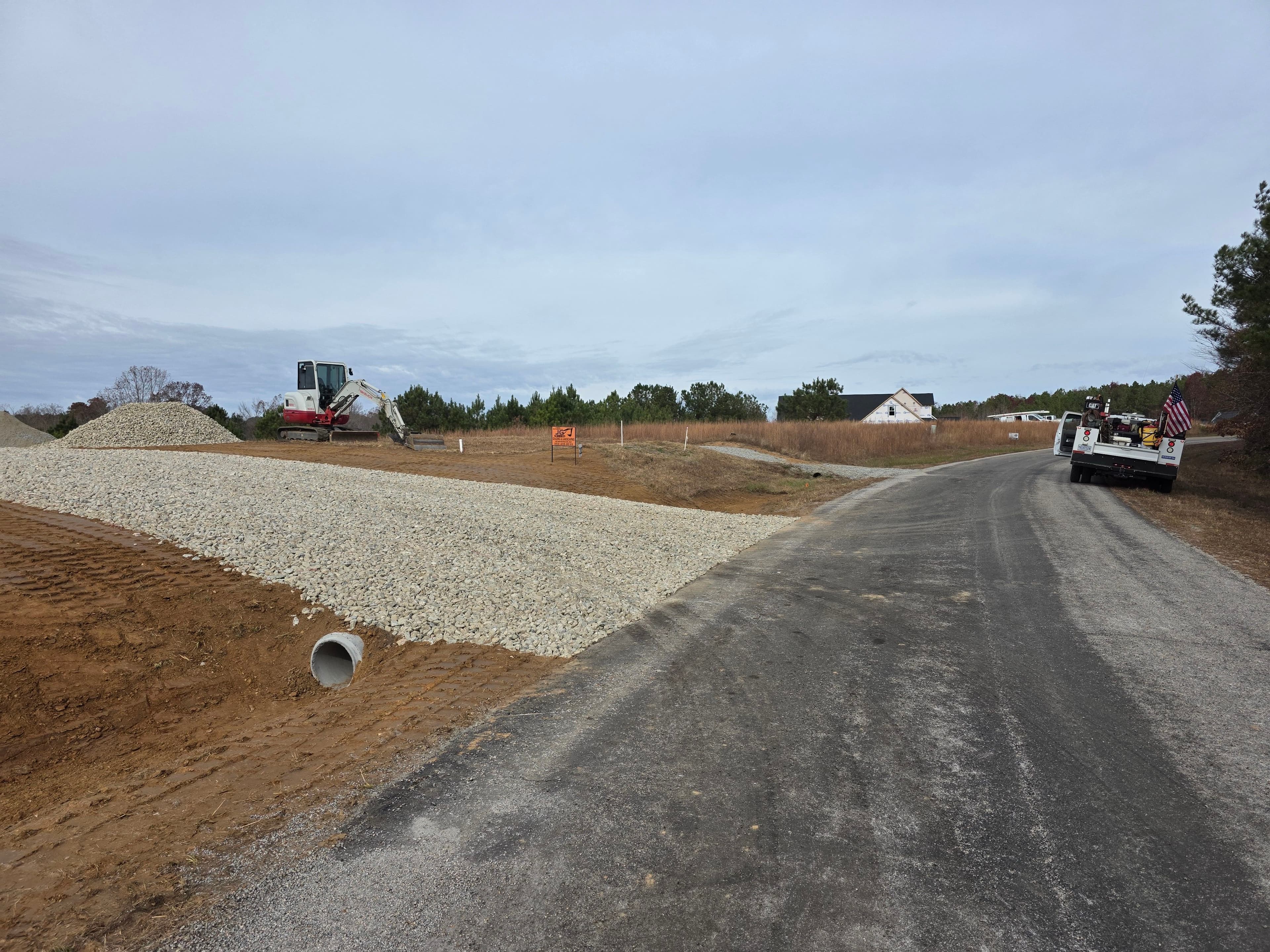 Construction site with gravel piles and machinery alongside a newly developed road.
