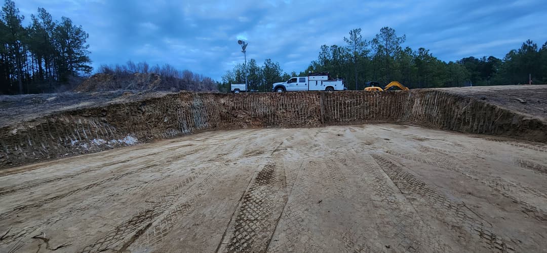 Excavated construction site with heavy machinery and cloudy sky in the background.