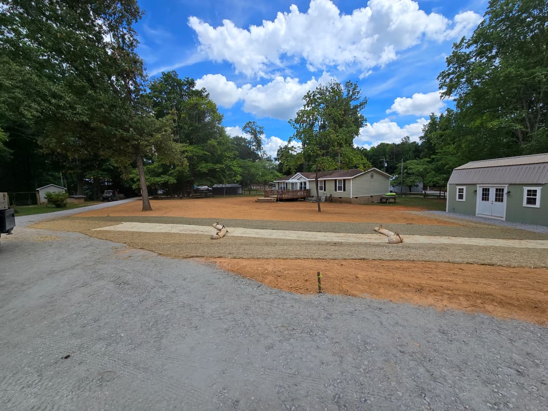Residential landscaping project with freshly prepared yard, gravel path, and trees under a blue sky.