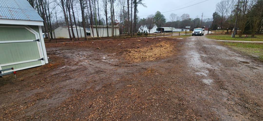 Cleared muddy lot with gravel road and trees in a residential area on a rainy day.