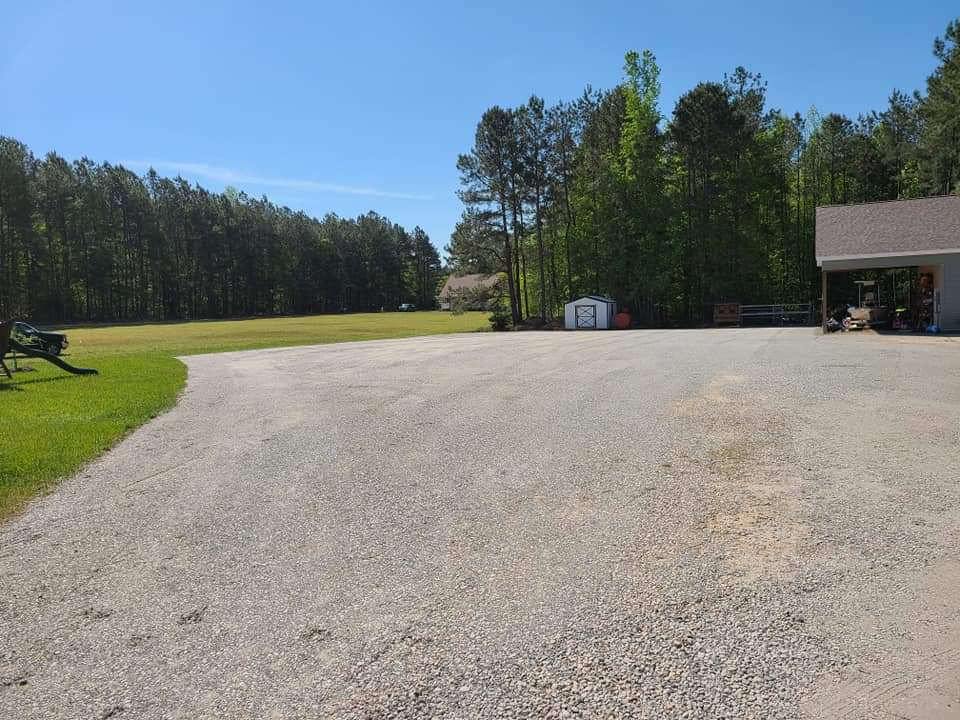 Spacious gravel area surrounded by trees, ideal for outdoor activities and parking.