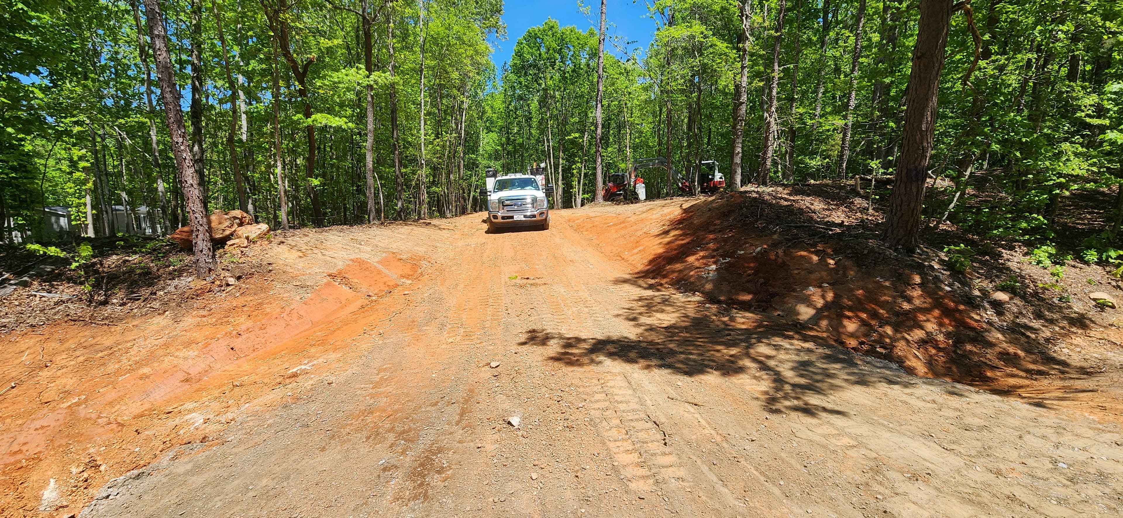Gravel road construction surrounded by lush green trees in a forested area.