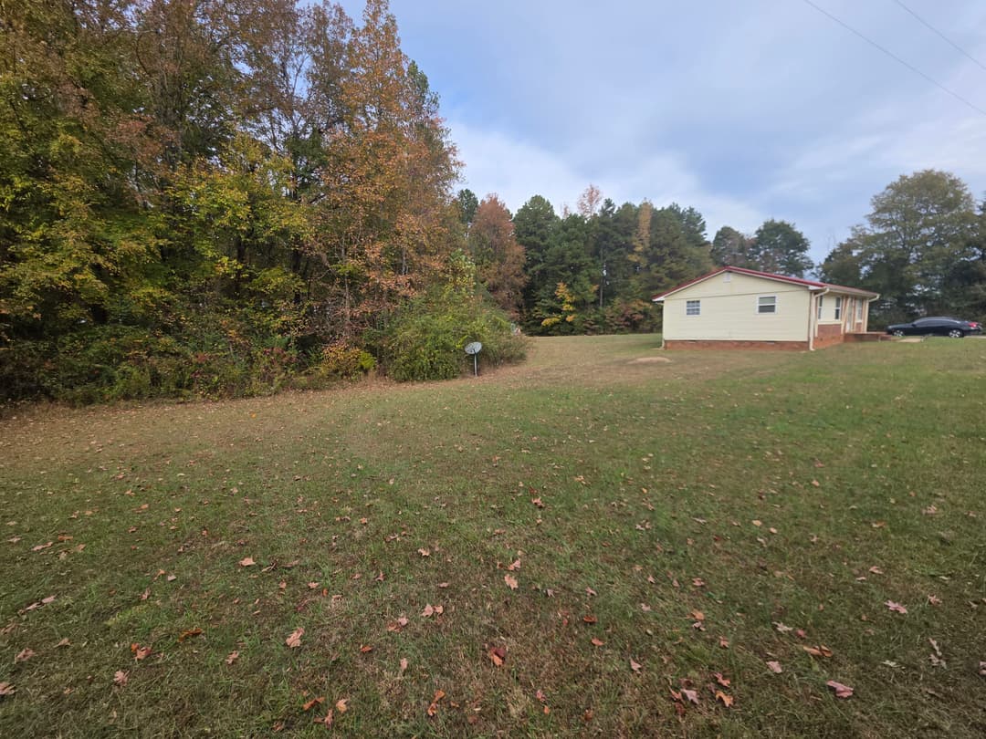 Rural home surrounded by autumn trees and grassy yard, satellite dish in view.