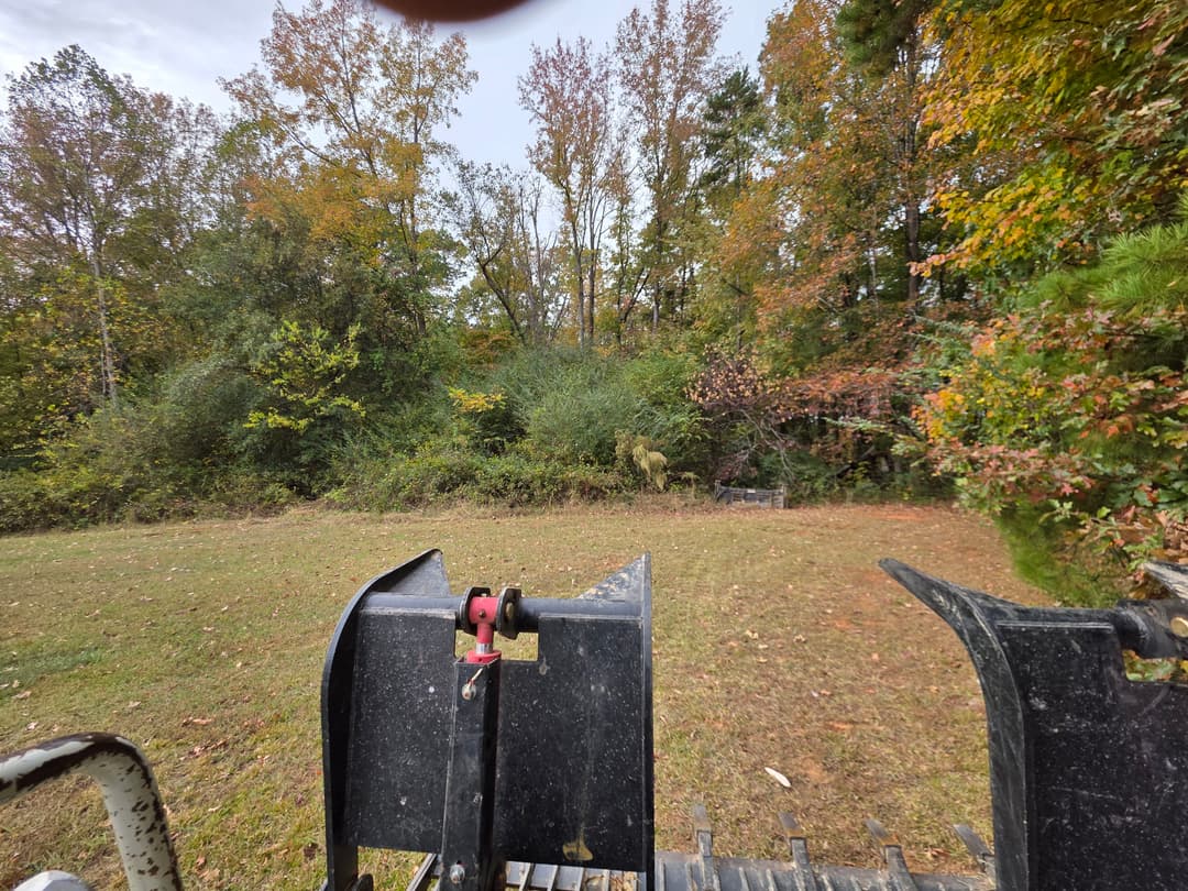 View from a tractor's front loader in a wooded area with autumn foliage.