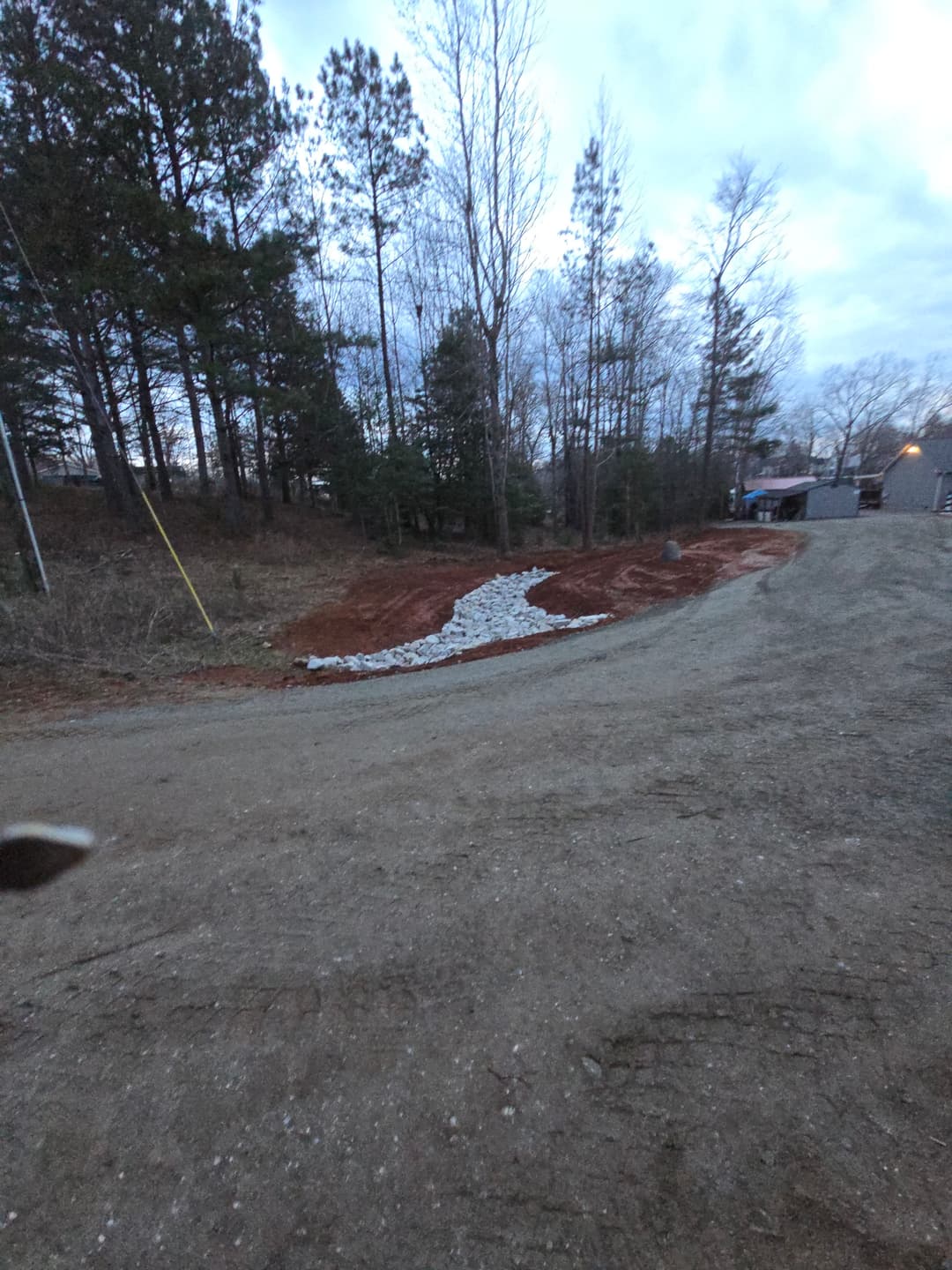 Gravel pathway through a wooded area at dusk, showcasing landscaping and natural surroundings.