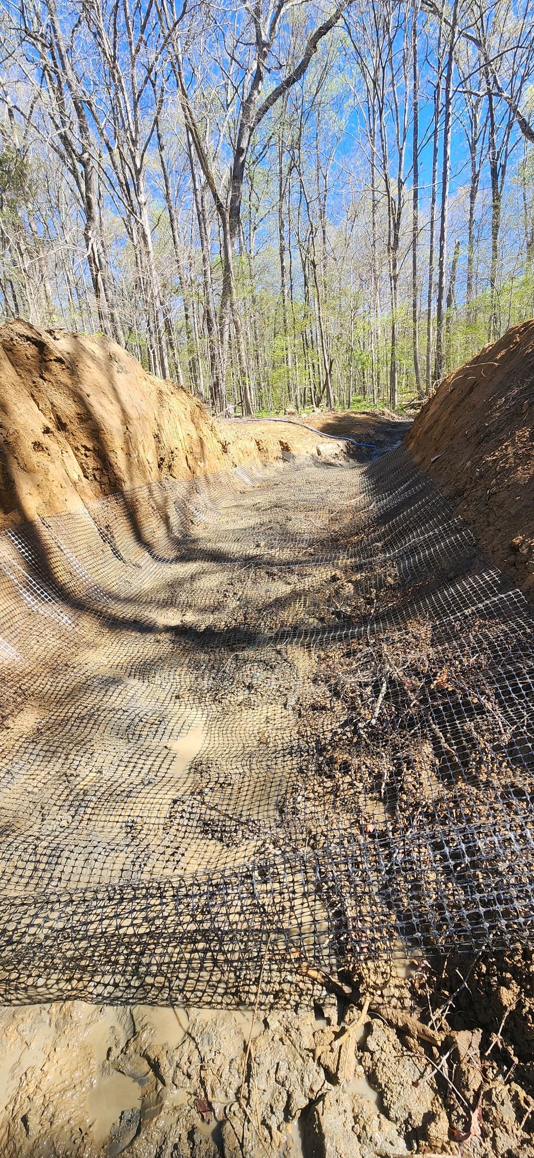 Erosion control netting along a dirt path in a forested area.