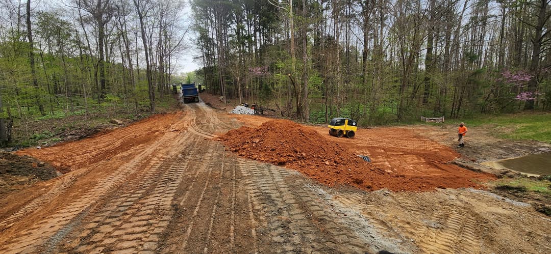 Construction site with earth movers reshaping a dirt road in a wooded area.