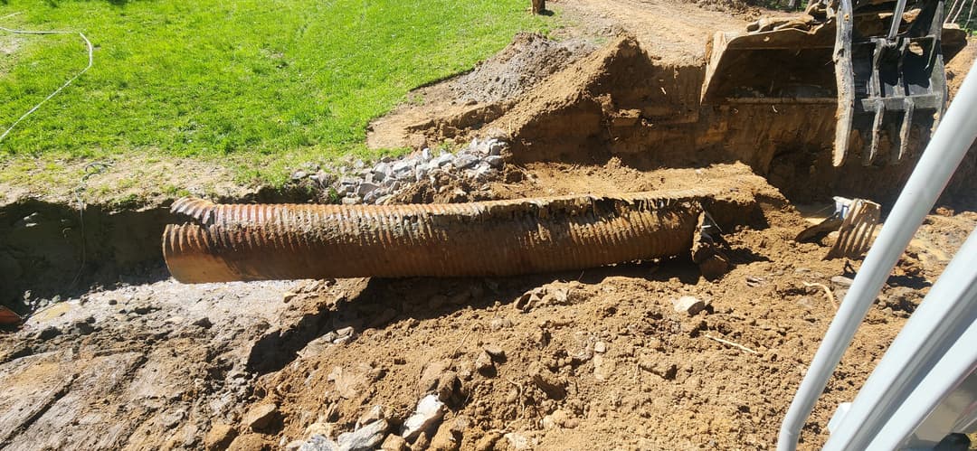 Excavation site showing a rusted metal pipe surrounded by dirt and construction equipment.