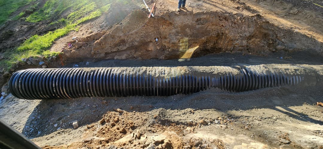 Construction site with underground drainage pipe installation on a sunny day.