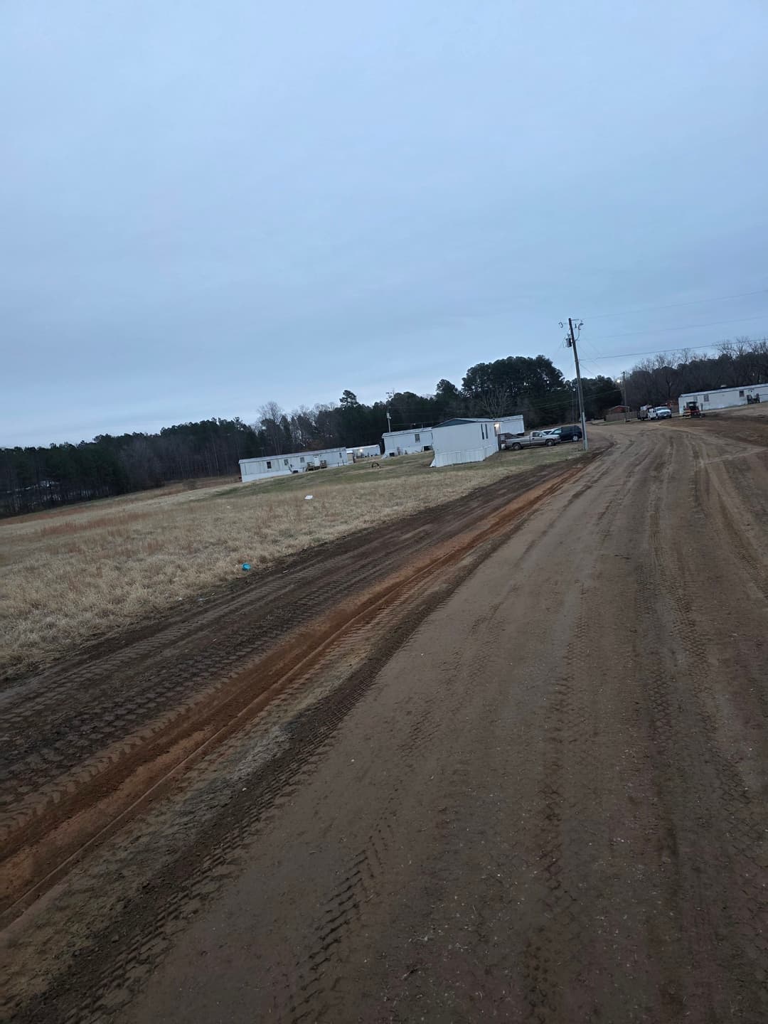 Dirt road leading to mobile homes on a cloudy day in a rural area.