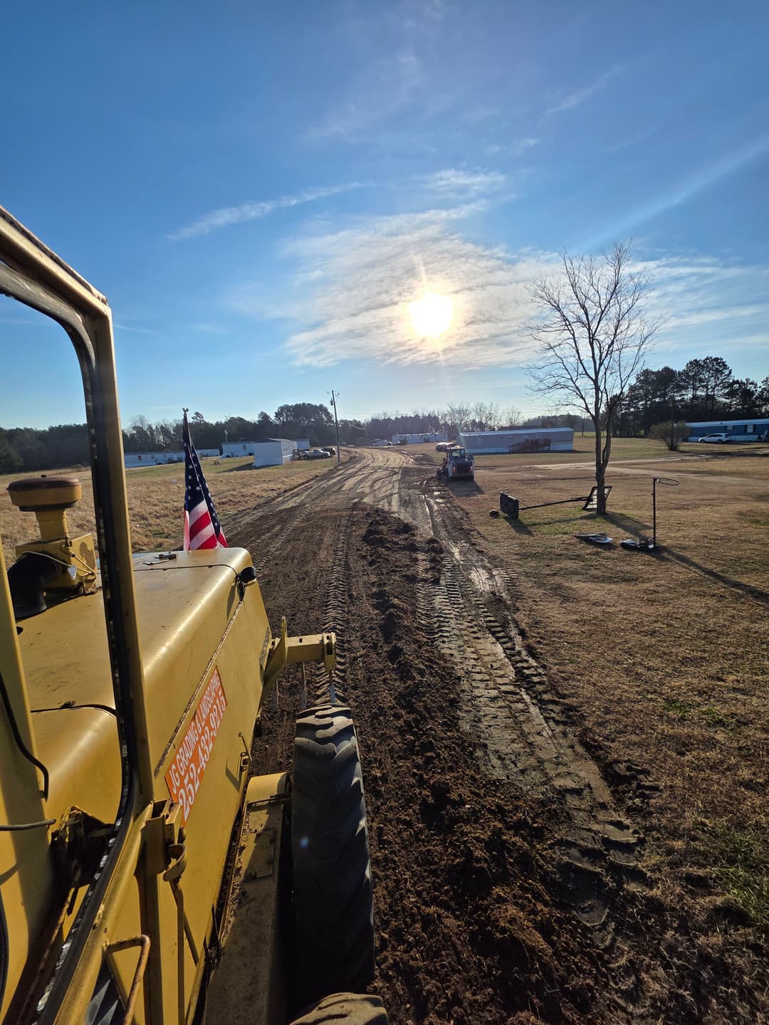 Bulldozer working on a construction site under a sunny sky, American flag visible.