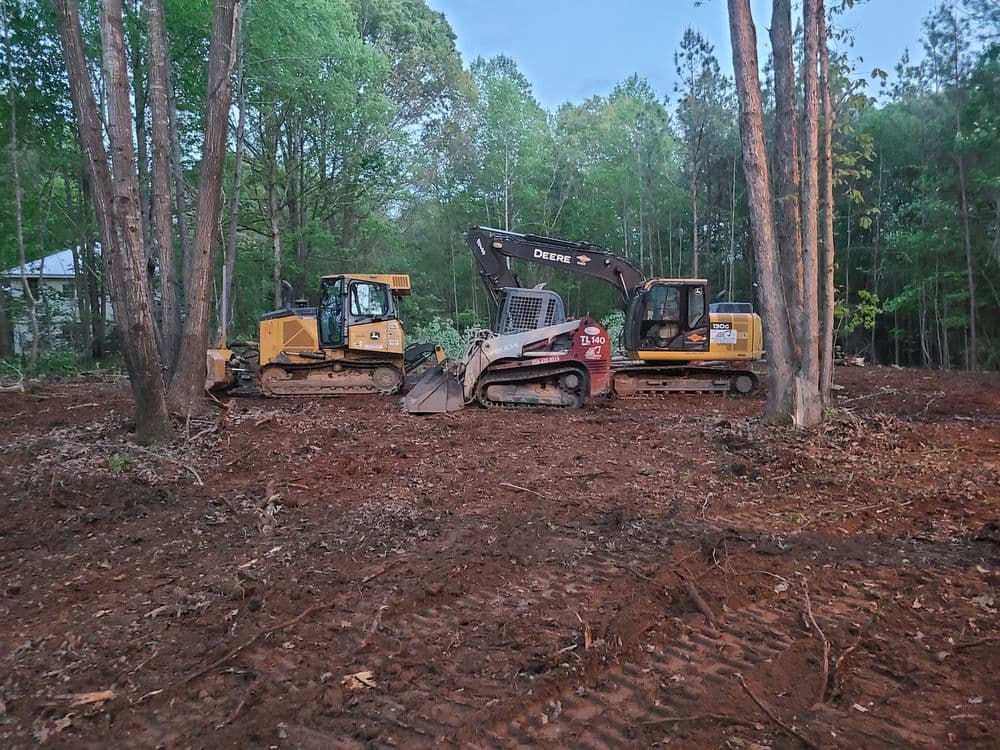 Excavators and bulldozer clearing land in a wooded area for development.