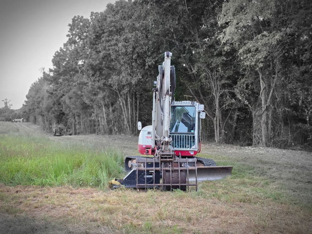Excavator in a grassy field, preparing for earth-moving construction work.